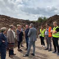 Menschen stehen vor den Hügeln einer Kompostierungsanlage