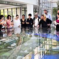 Menschen stehen in einem Gebäude und einen Glaskasten mit einer Modellanlage herum